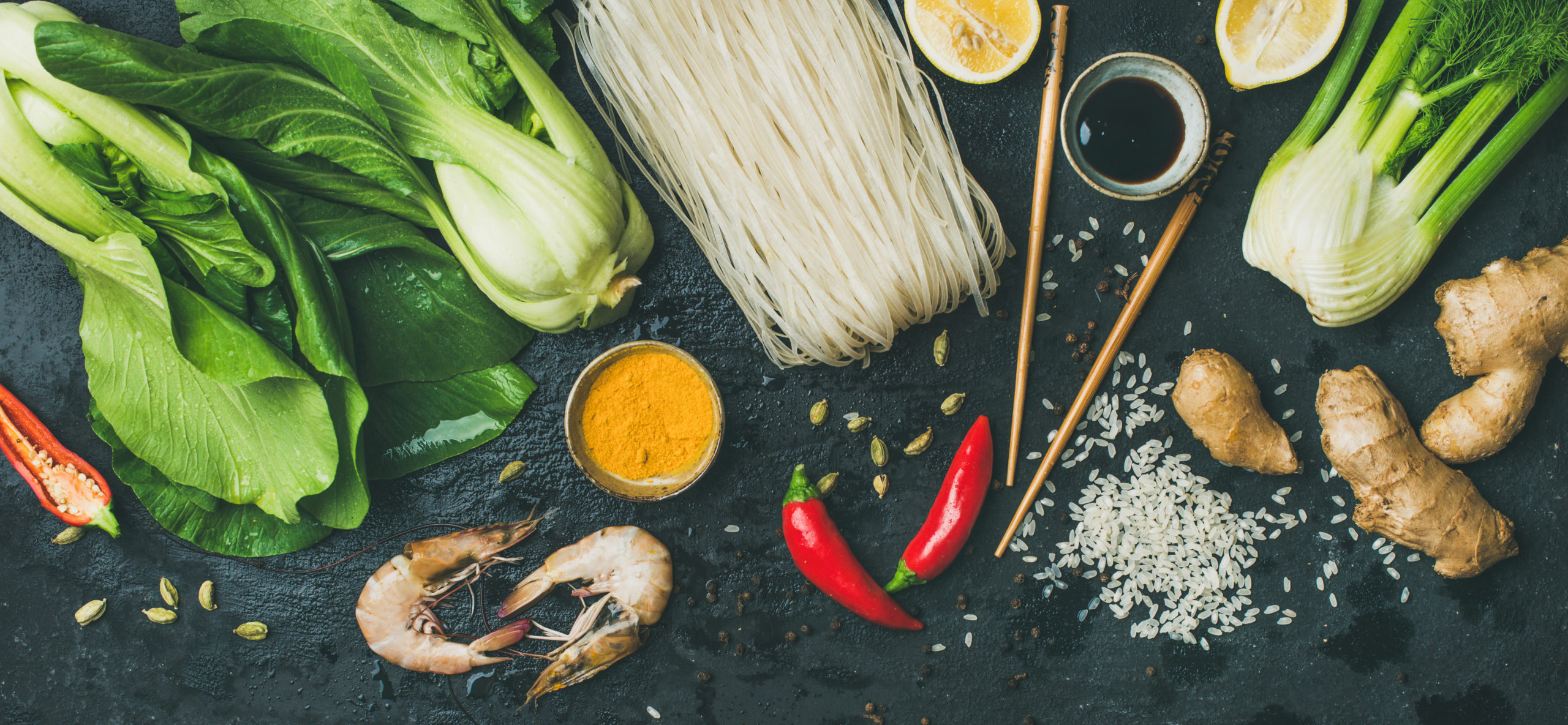 Asian cuisine ingredients over dark slate stone background, top view. Vegetables, spices, shrimp, rice, sauces for cooking vietnamese, thai or chinese food. Clean eating food concept